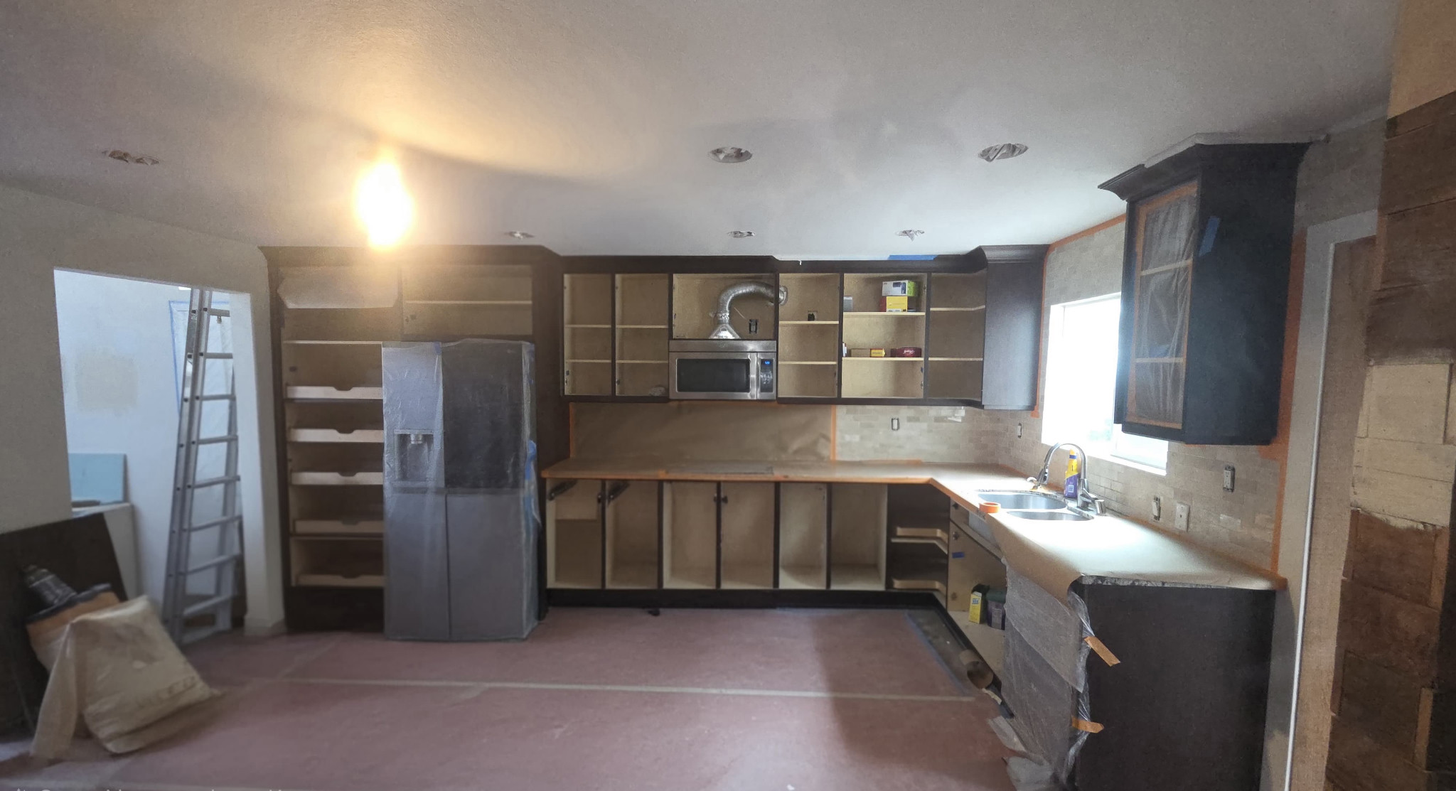 Kitchen before completion, with cabinet doors and drawer fronts removed and nearby surfaces protected.