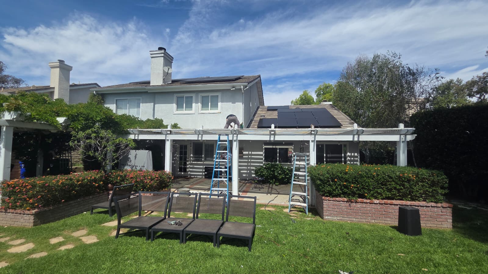 Rear house exterior and patio pergola with ladders in place during painting work