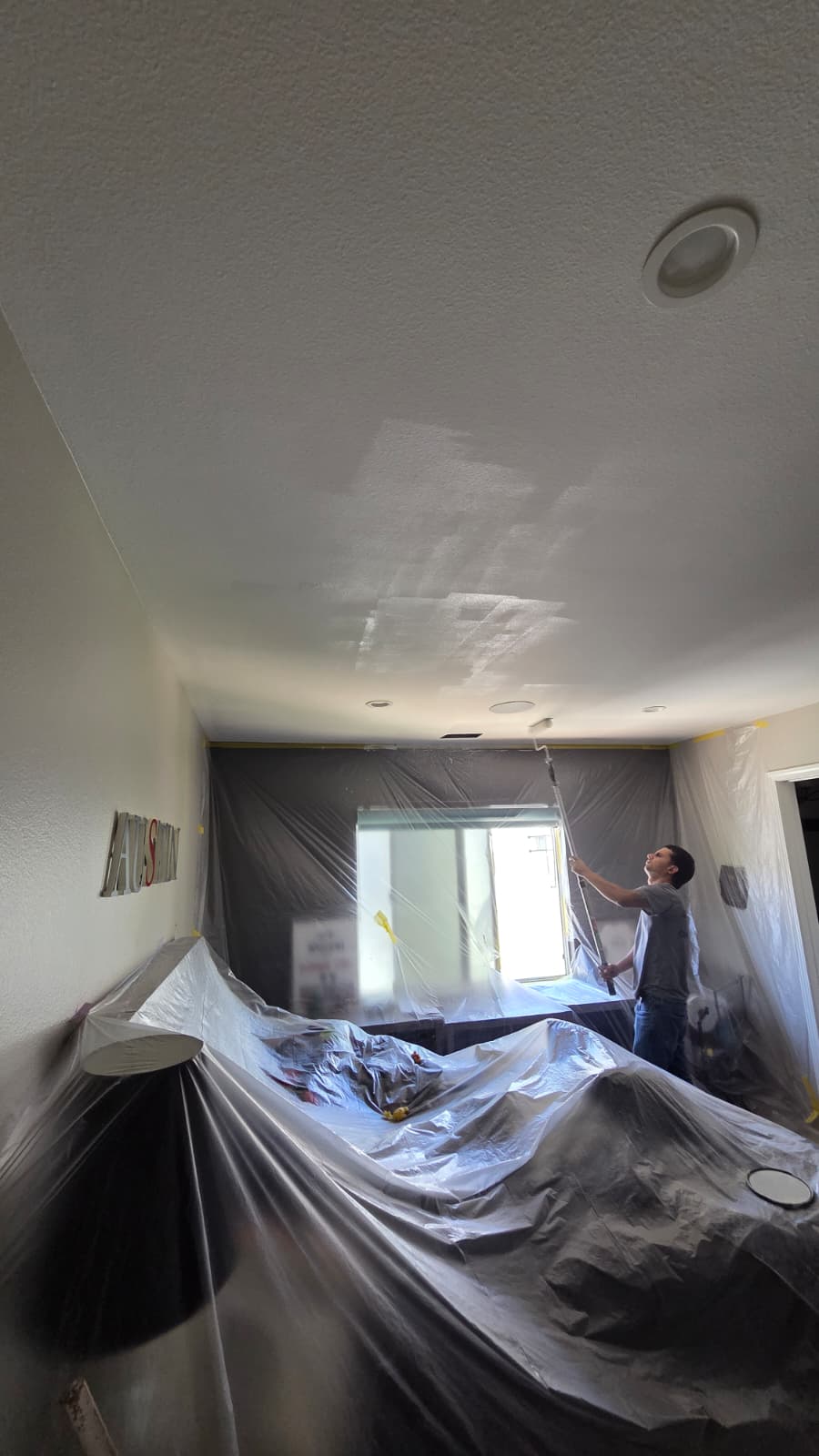 Painter rolling paint on an interior ceiling with the room covered in protective plastic