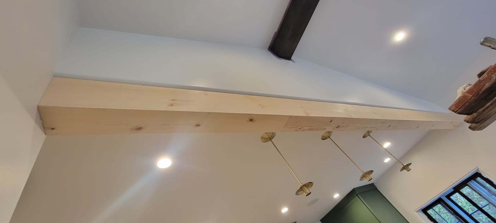 Unfinished light wood ceiling beam installed against a white vaulted ceiling before staining