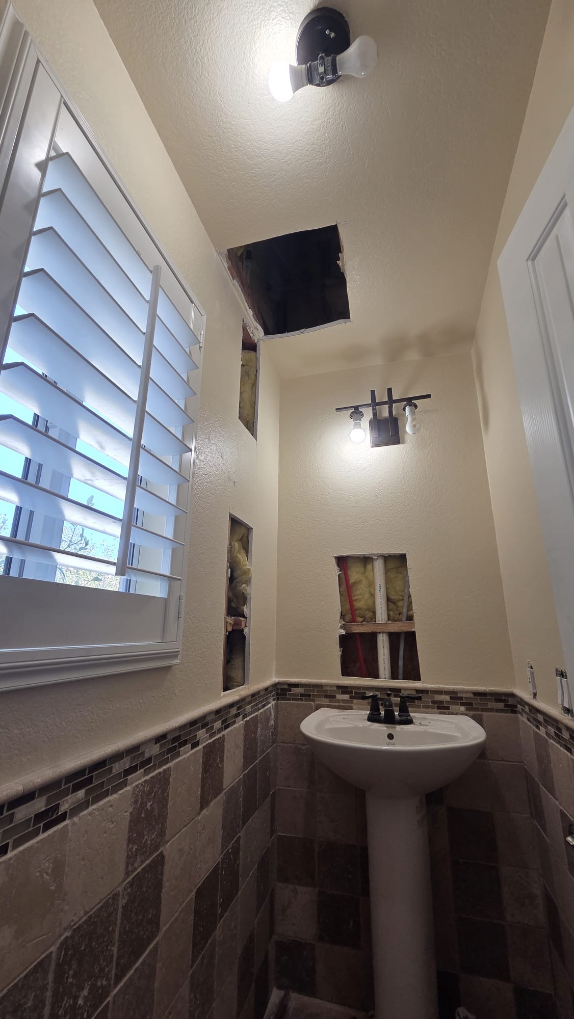 Openings in the bathroom ceiling and wall near the sink during drywall repair