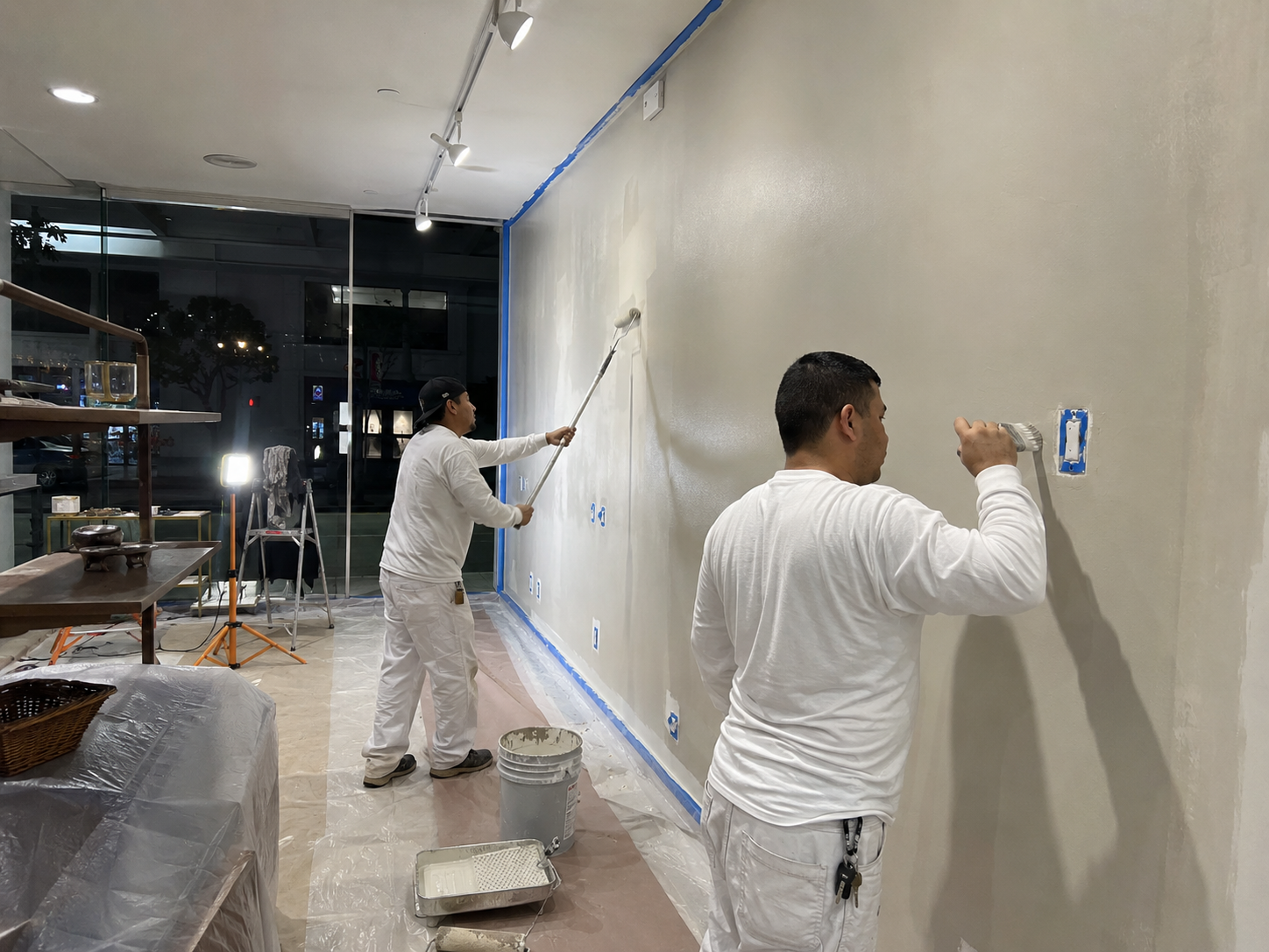 Painters rolling and patching walls inside a commercial storefront space